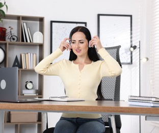 Photo of Woman in headphones passing online test via laptop at table indoors