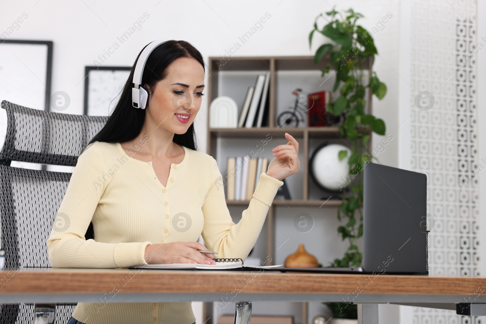 Photo of Woman in headphones passing online test via laptop at table indoors