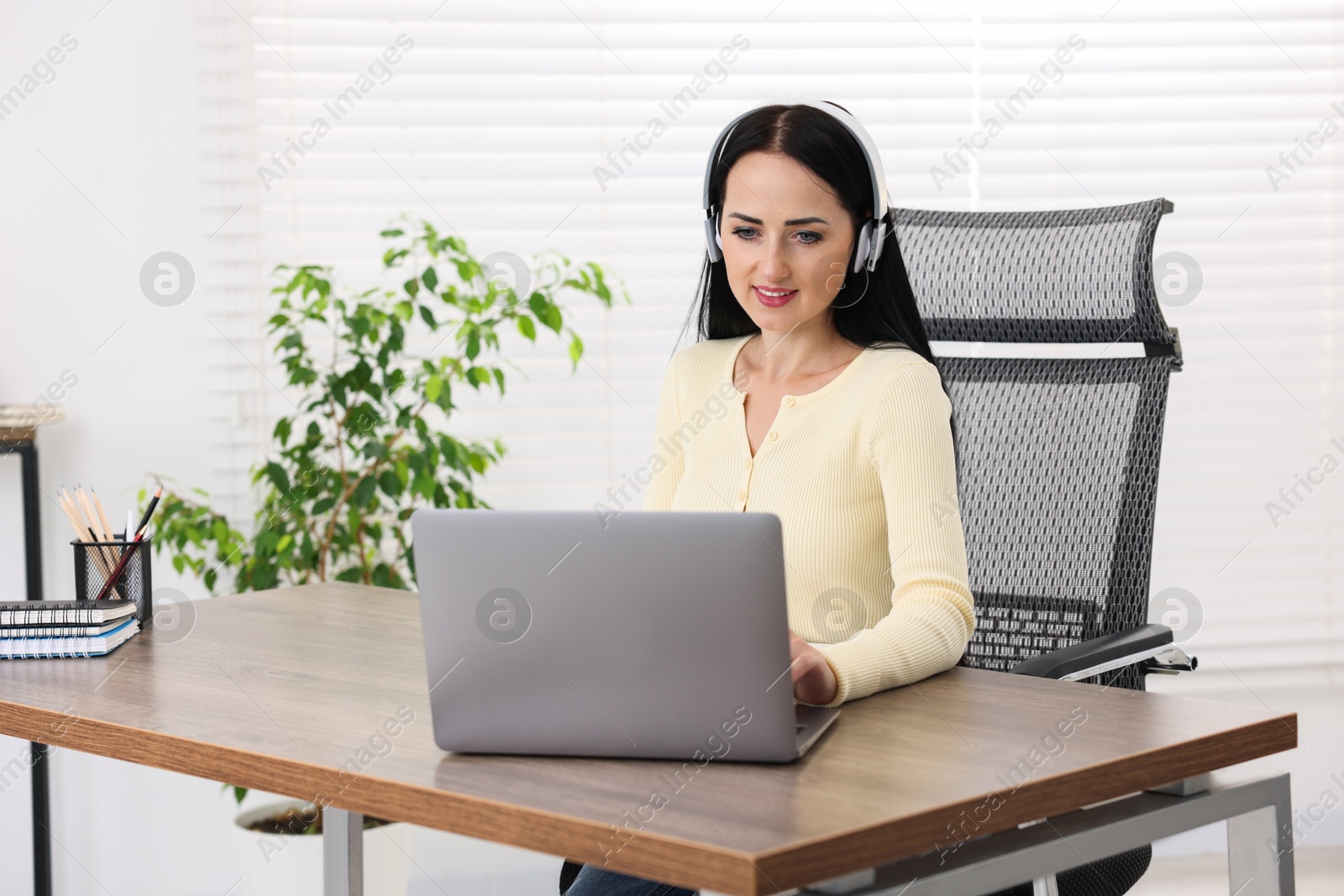 Photo of Woman in headphones passing online test via laptop at table indoors