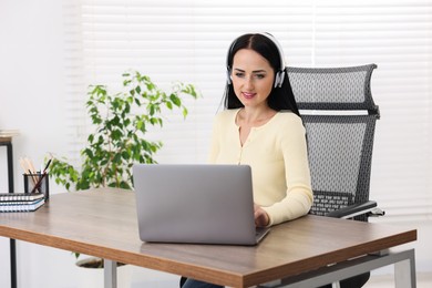 Photo of Woman in headphones passing online test via laptop at table indoors