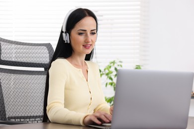 Photo of Woman in headphones passing online test via laptop at table indoors