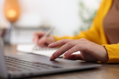 Photo of Woman taking notes while passing online test via laptop at table indoors, closeup