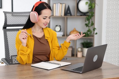 Photo of Woman in headphones passing online test via laptop at table indoors