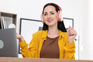 Photo of Woman in headphones passing online test via laptop at table indoors