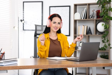 Photo of Woman in headphones passing online test via laptop at table indoors