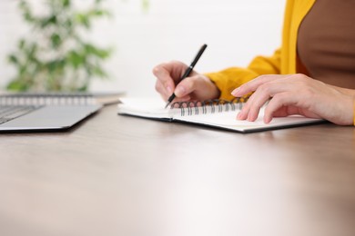 Photo of Woman taking notes while passing online test via laptop at table indoors, closeup