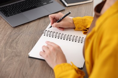 Photo of Woman taking notes while passing online test via laptop at table indoors, closeup