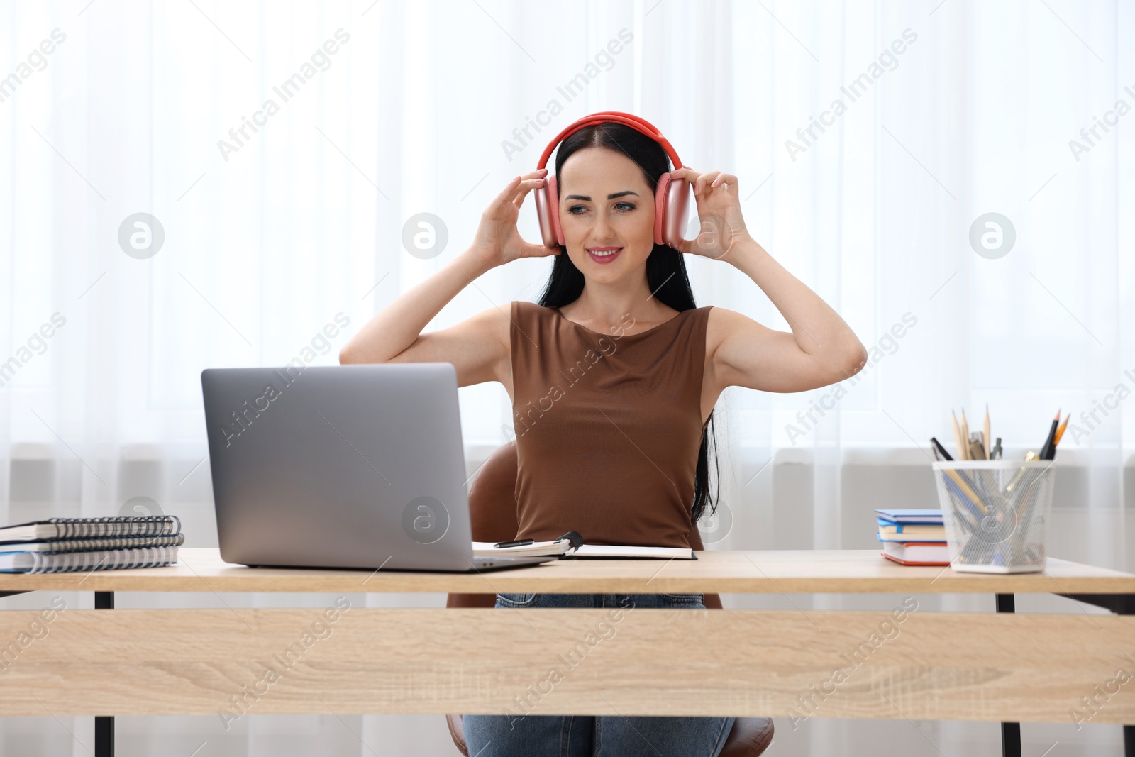 Photo of Woman in headphones passing online test via laptop at table indoors