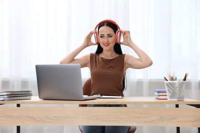 Photo of Woman in headphones passing online test via laptop at table indoors