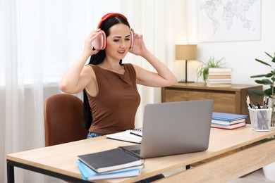 Photo of Woman in headphones passing online test via laptop at table indoors