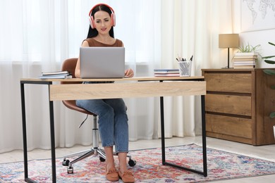 Photo of Woman in headphones passing online test via laptop at table indoors
