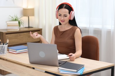 Photo of Woman in headphones passing online test via laptop at table indoors