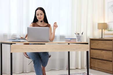 Photo of Woman in headset passing online test on laptop at table indoors