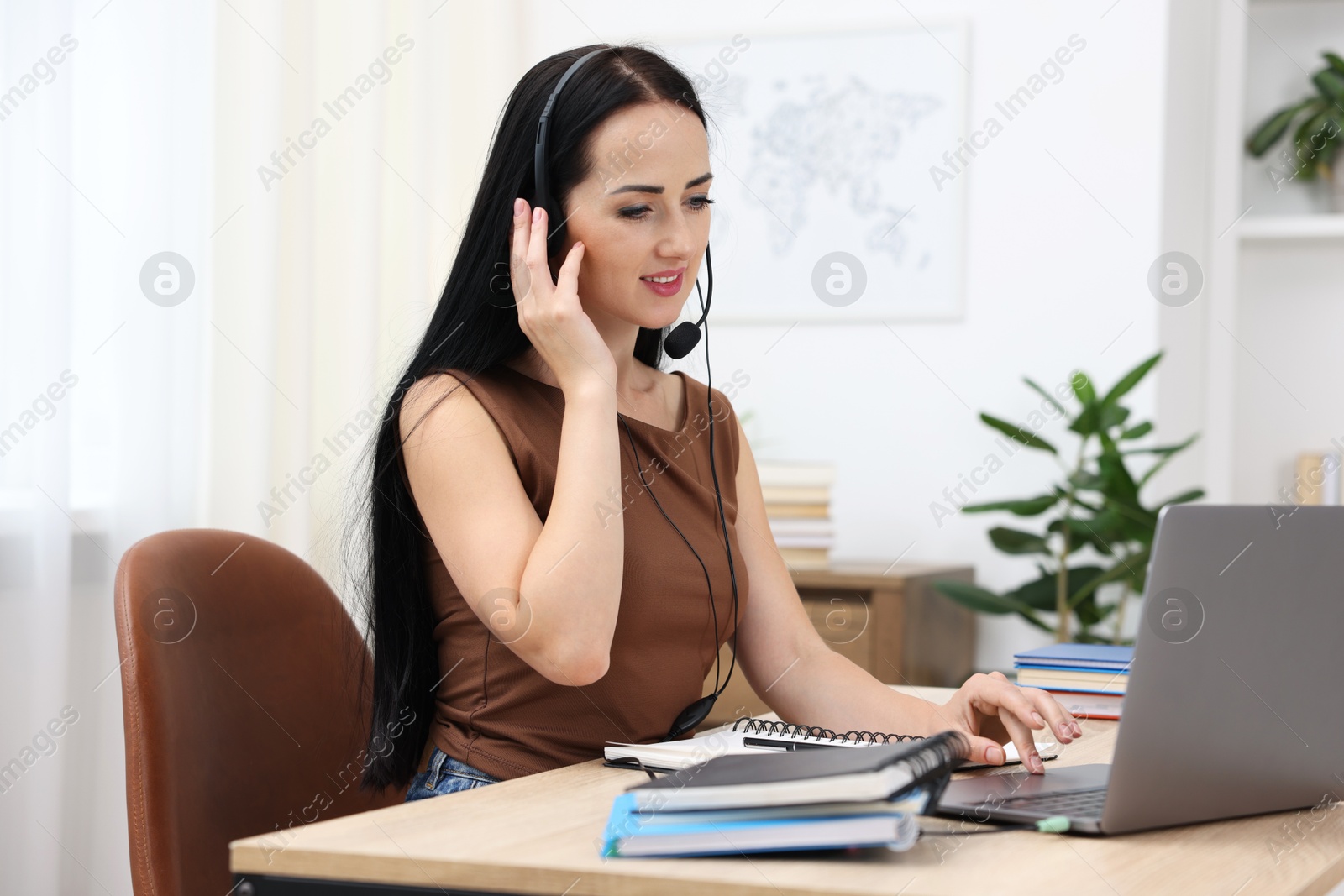 Photo of Woman in headset passing online test on laptop at table indoors
