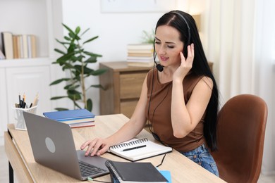 Photo of Woman in headset passing online test on laptop at table indoors