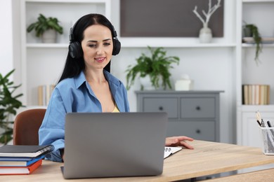 Photo of Woman in headphones passing online test on laptop at table indoors