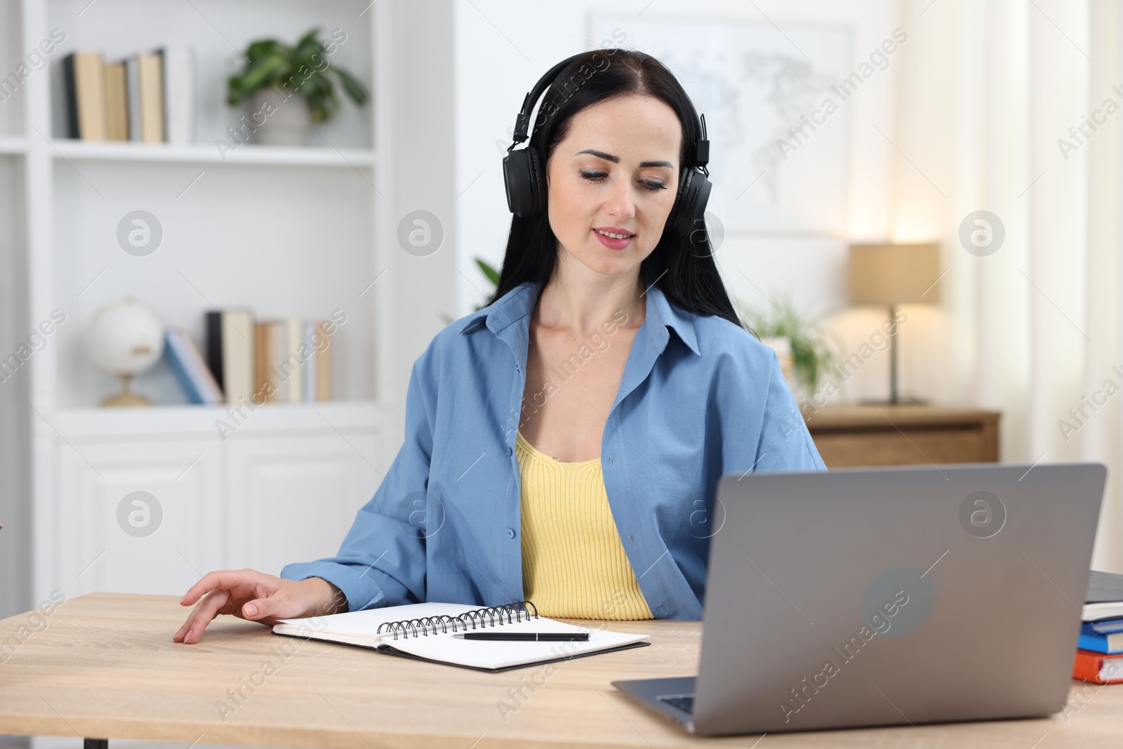 Photo of Woman in headphones passing online test on laptop at table indoors