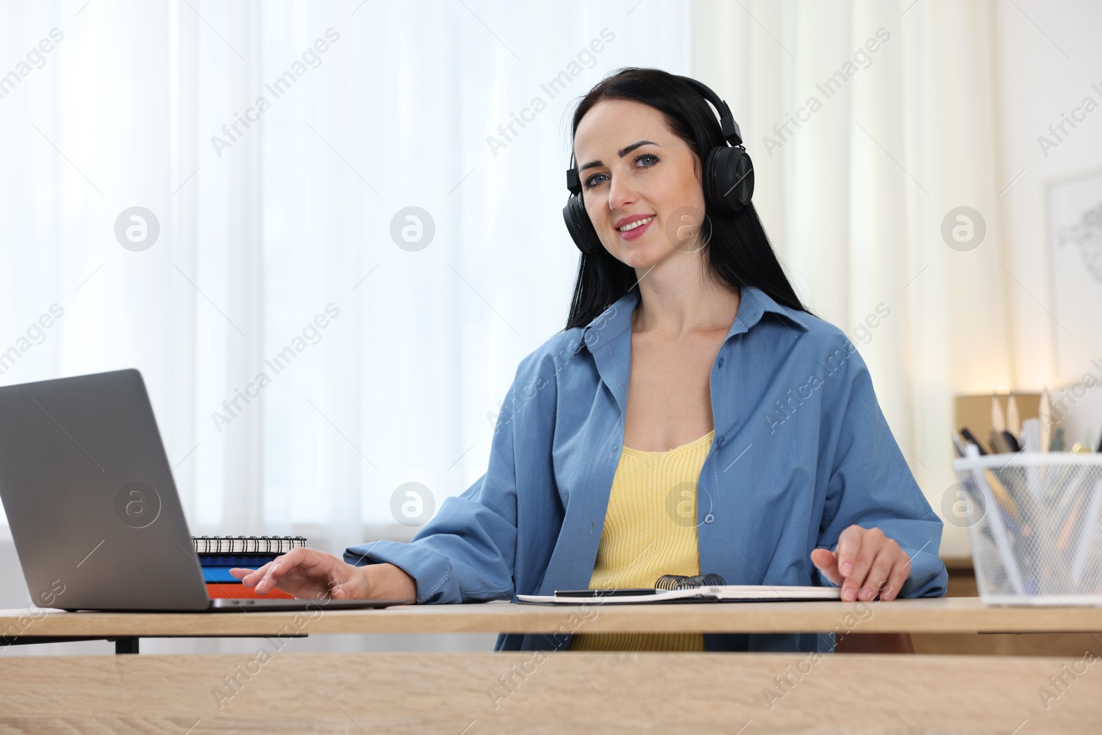 Photo of Woman in headphones passing online test on laptop at table indoors