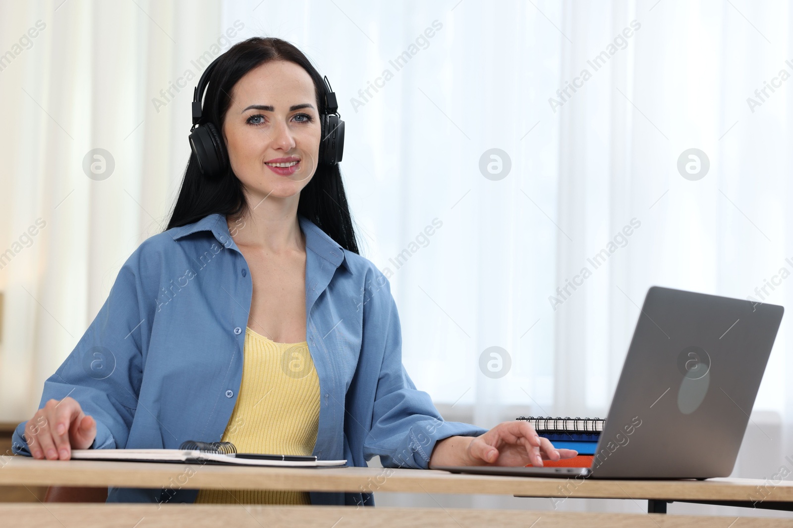 Photo of Woman in headphones passing online test on laptop at table indoors