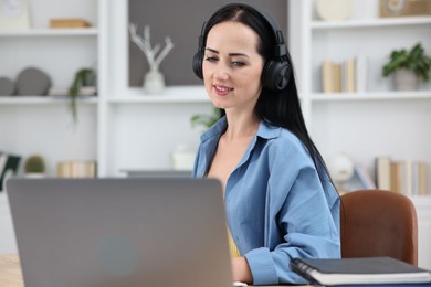 Photo of Woman in headphones passing online test via laptop at table indoors