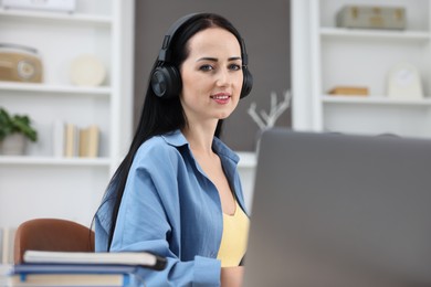 Photo of Woman in headphones passing online test via laptop indoors