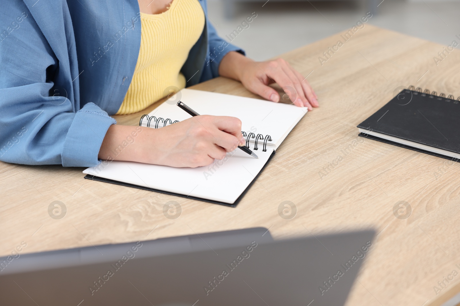 Photo of Woman taking notes while passing online test via laptop at wooden table indoors, closeup