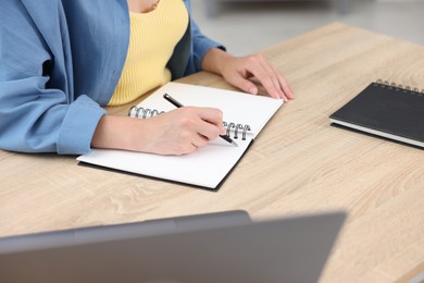 Photo of Woman taking notes while passing online test via laptop at wooden table indoors, closeup