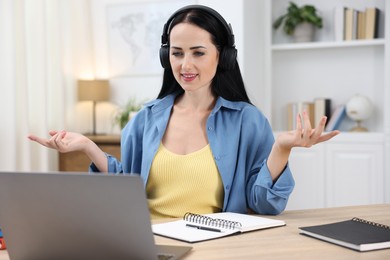 Photo of Woman in headphones passing online test via laptop at table indoors