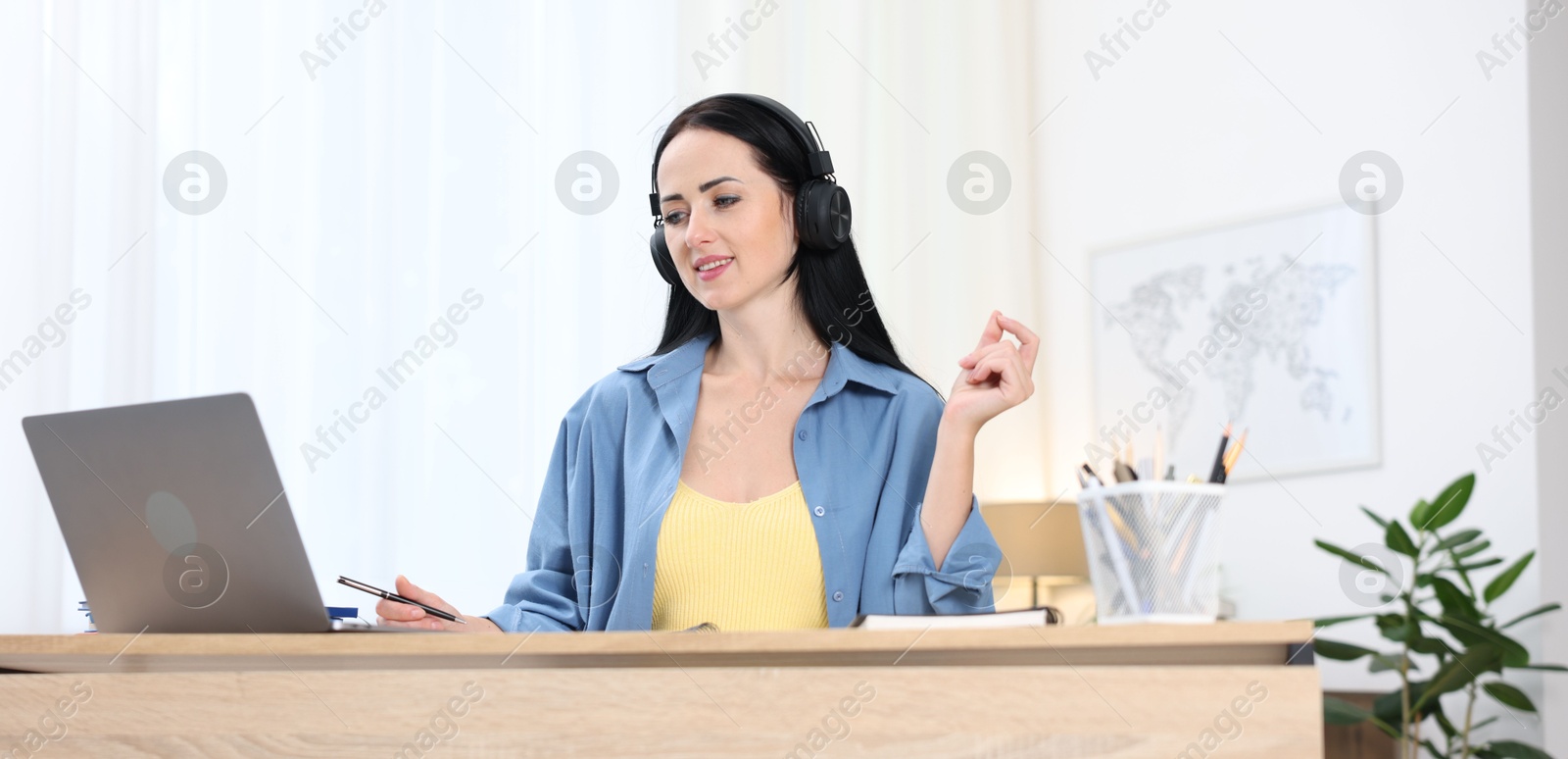 Photo of Woman in headphones passing online test via laptop at table indoors