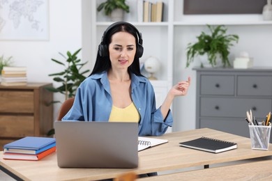 Photo of Woman in headphones passing online test via laptop at table indoors
