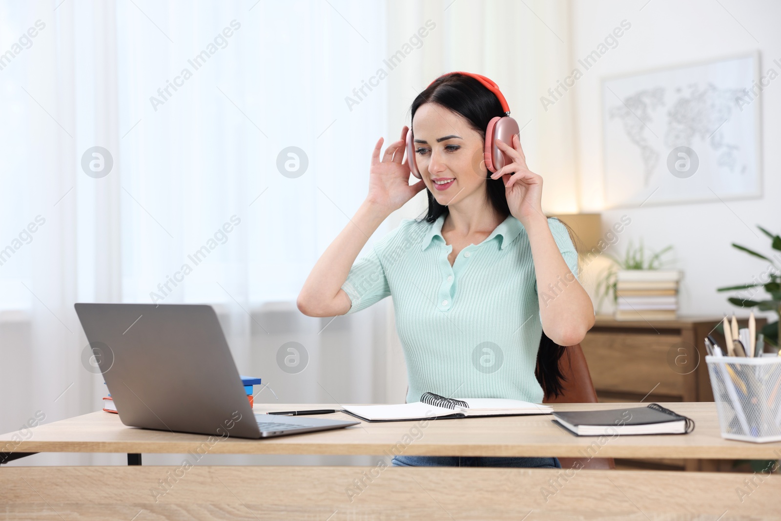 Photo of Woman in headphones passing online test via laptop at table indoors