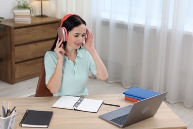Photo of Woman in headphones passing online test via laptop at table indoors