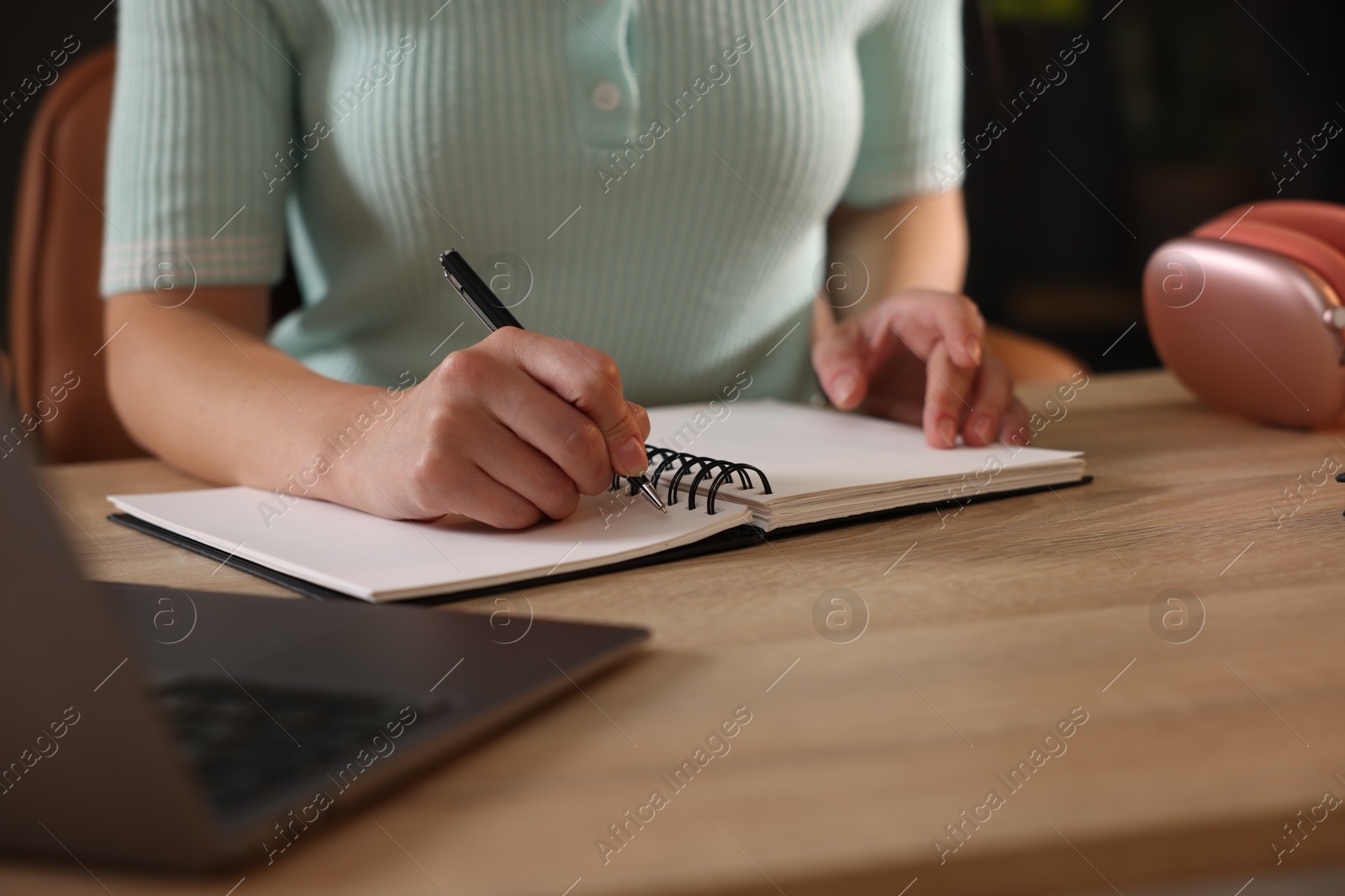 Photo of Woman taking notes while passing online test via laptop at wooden table indoors, closeup