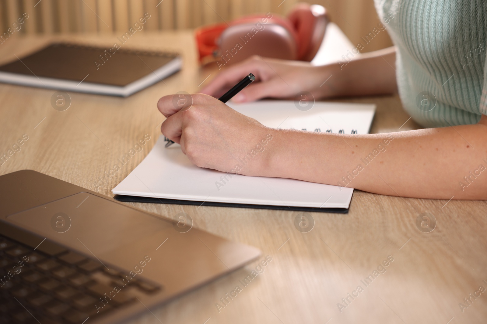 Photo of Woman taking notes while passing online test via laptop at wooden table indoors, closeup