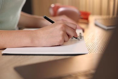 Photo of Woman taking notes while passing online test via laptop at wooden table indoors, closeup
