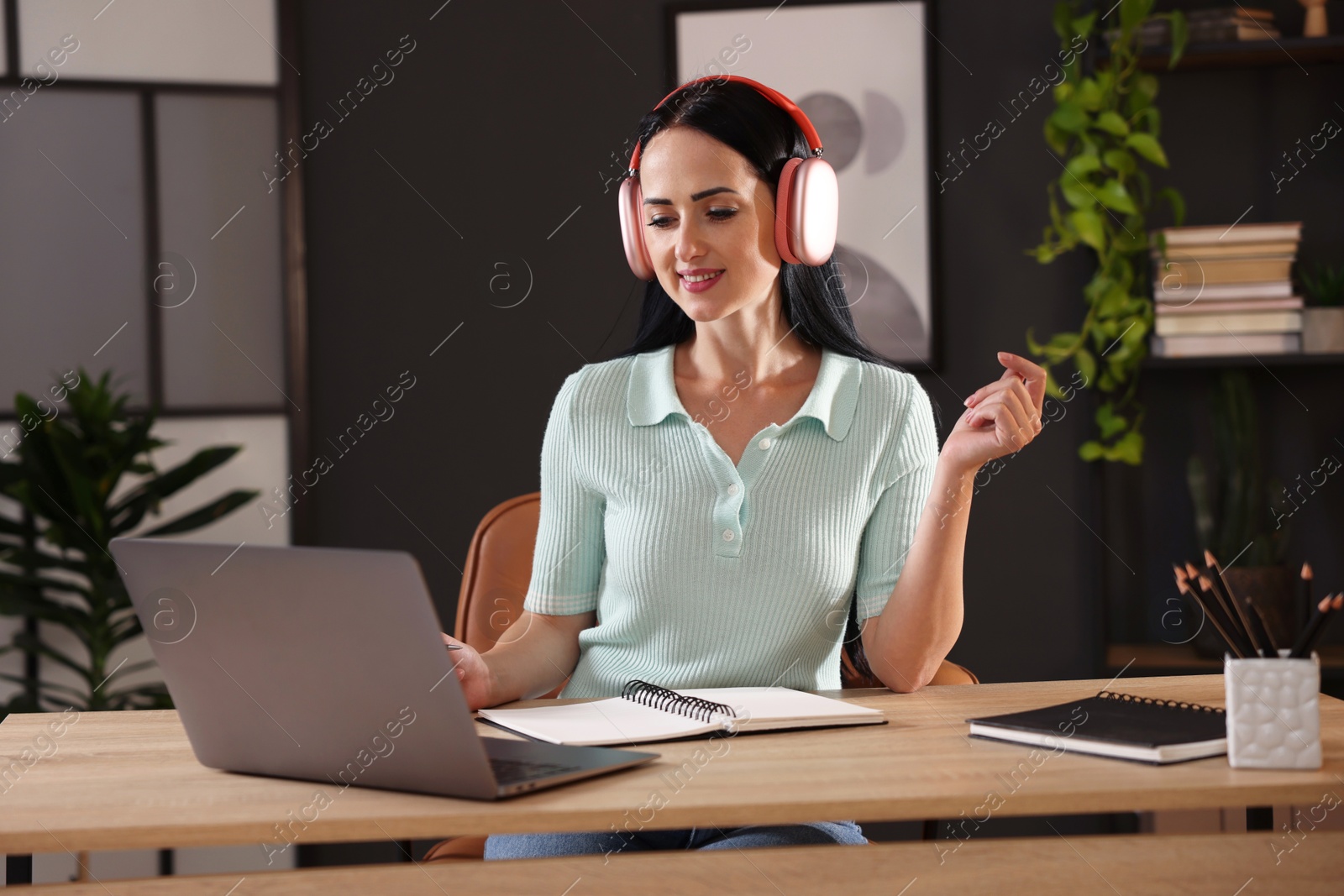 Photo of Woman in headphones passing online test via laptop at table indoors