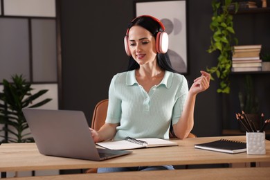 Photo of Woman in headphones passing online test via laptop at table indoors