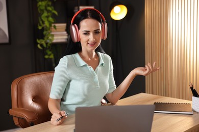 Photo of Woman in headphones passing online test via laptop at table indoors