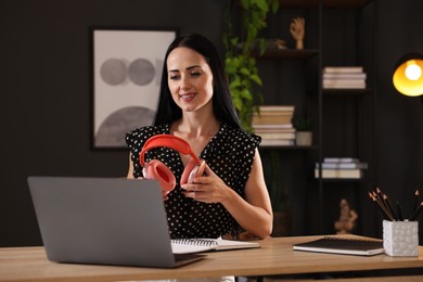 Photo of Woman with headphones passing online test via laptop at table indoors