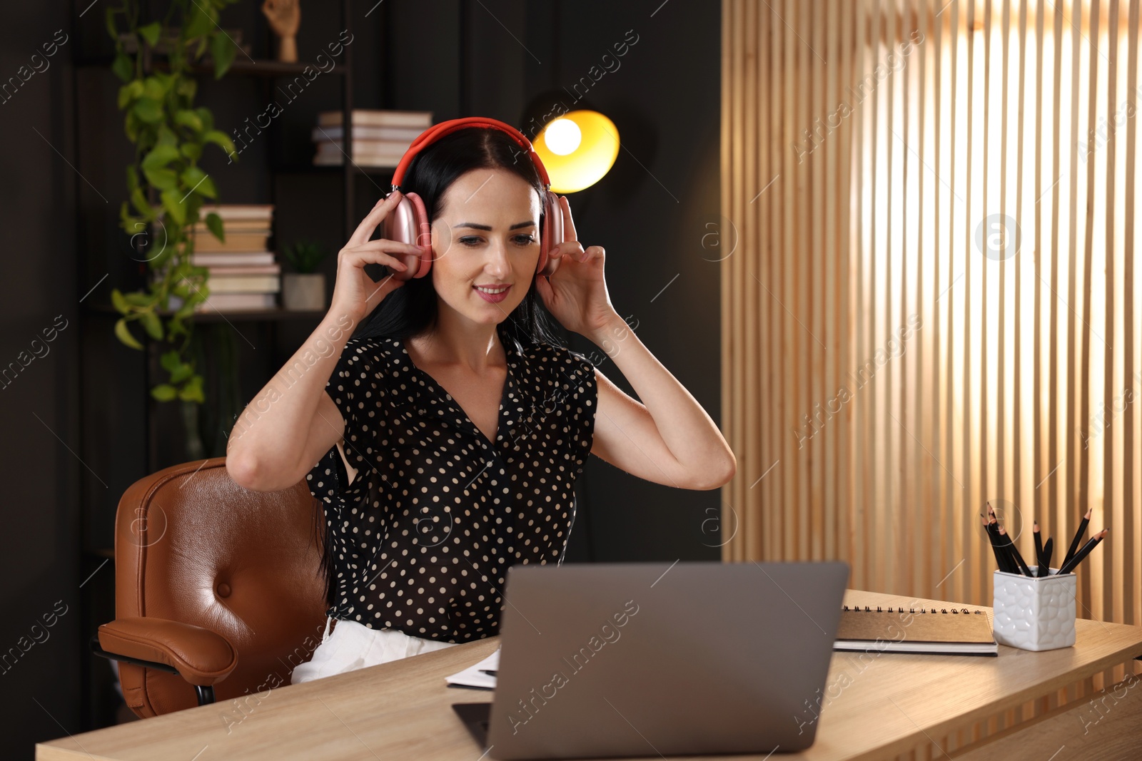 Photo of Woman in headphones passing online test via laptop at table indoors