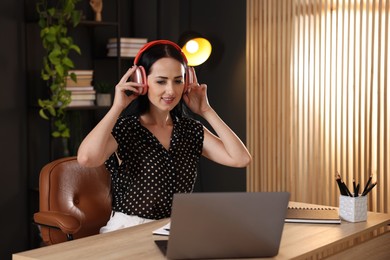 Photo of Woman in headphones passing online test via laptop at table indoors