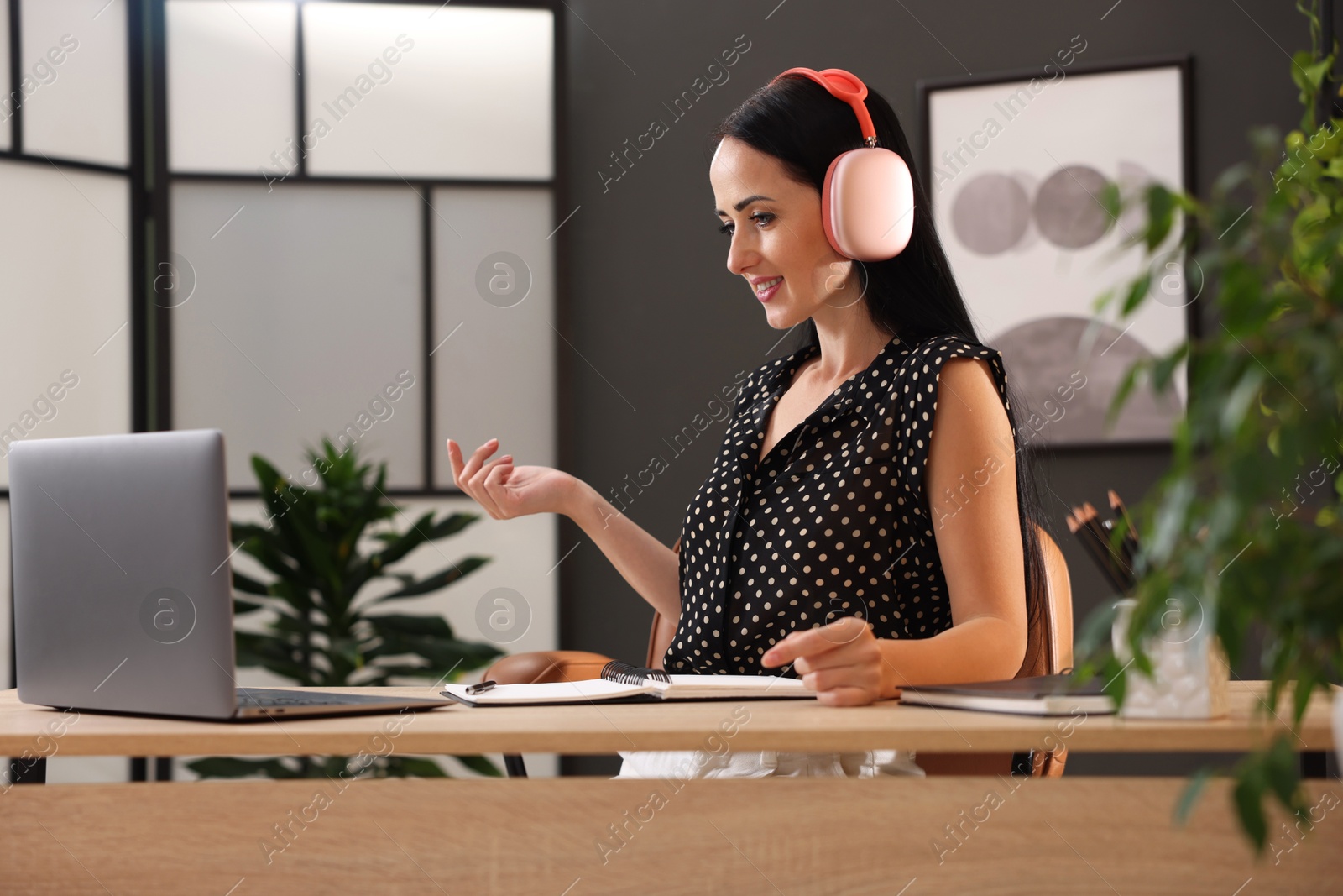 Photo of Woman in headphones passing online test via laptop at table indoors