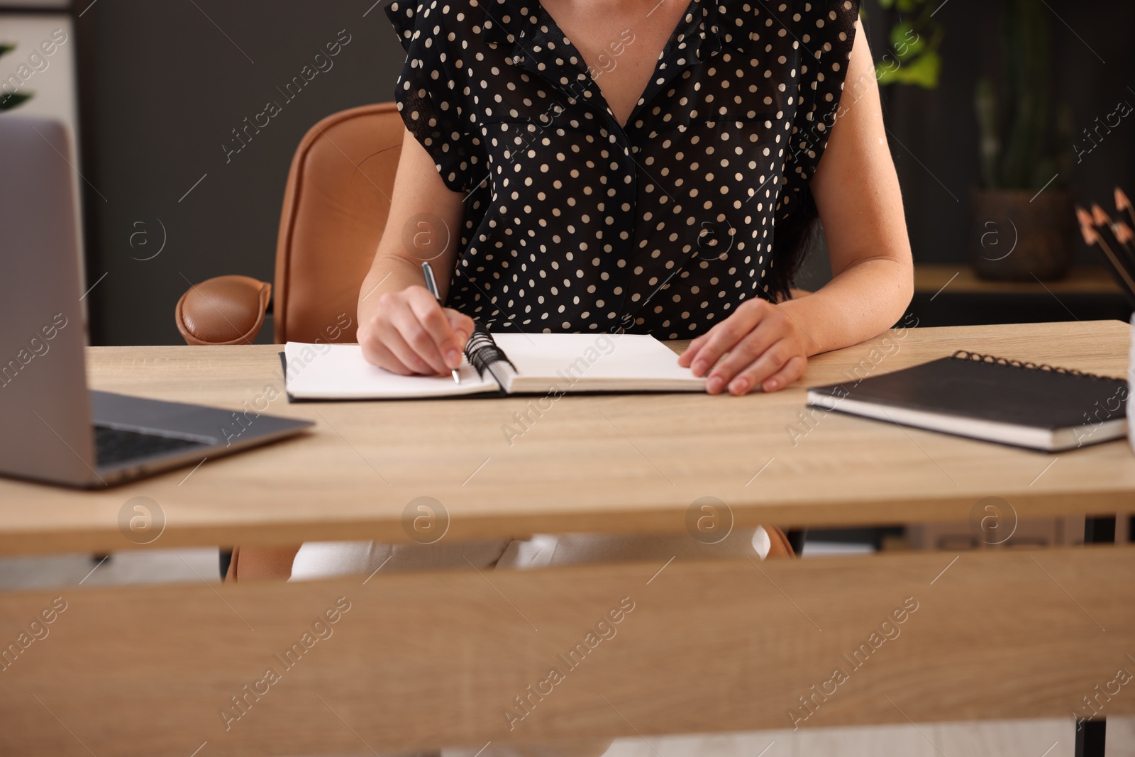 Photo of Woman taking notes while passing online test via laptop at table indoors, closeup