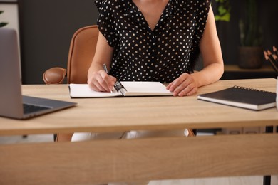 Photo of Woman taking notes while passing online test via laptop at table indoors, closeup