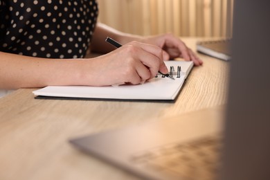 Photo of Woman taking notes while passing online test via laptop at table indoors, closeup