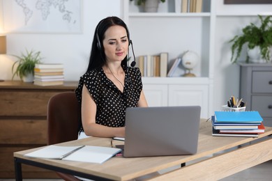 Photo of Woman in headset passing online test via laptop at table indoors