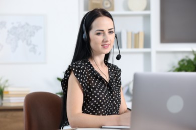 Photo of Woman in headset passing online test via laptop at table indoors