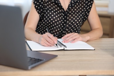 Photo of Woman taking notes while passing online test via laptop at table indoors, closeup