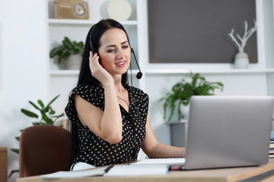 Photo of Woman in headset passing online test via laptop at table indoors