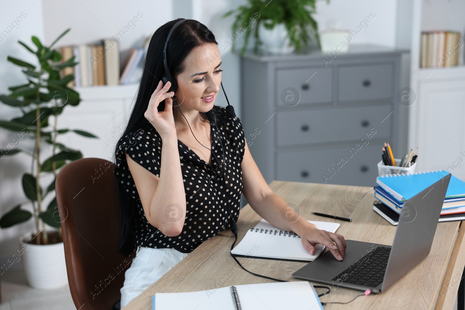 Photo of Woman in headset passing online test on laptop at table indoors